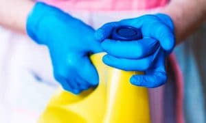 A ladies gloved hands, twisting the cap of a large yellow bottle of bleach