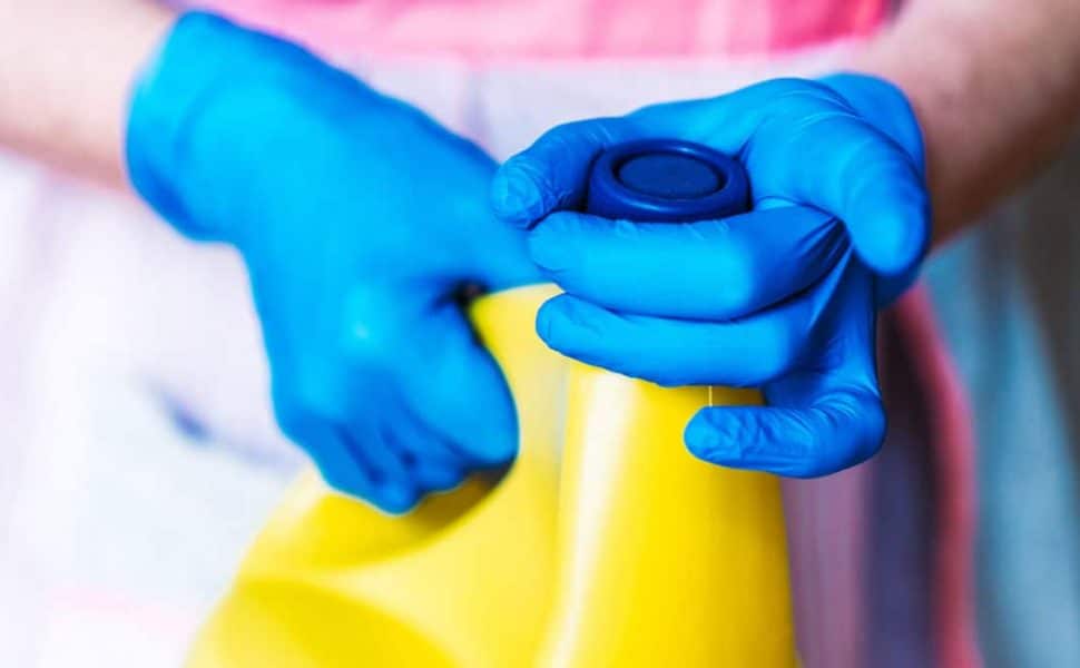 A ladies gloved hands, twisting the cap of a large yellow bottle of bleach