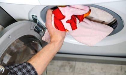A man putting some red and white clothes into a dryer