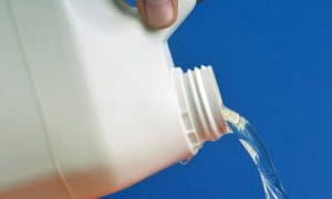 Bleach being poured from a white bottle against a blue background